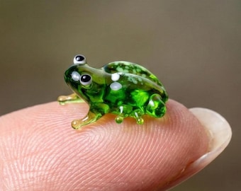 May include: A miniature glass frog figurine in a vibrant translucent green hue. The small sculpture features white spotted markings on its back and two distinct black and white eyes, crafted with smooth, rounded edges and a glossy finish.