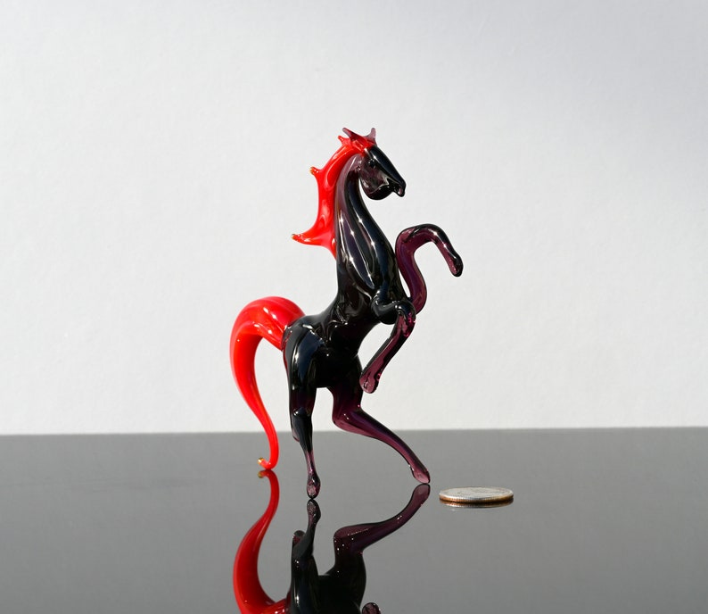 Peut inclure: Une figurine de cheval en verre noir avec une crini&egrave;re et une queue rouges. Le cheval est debout sur ses pattes arri&egrave;re, les pattes avant lev&eacute;es. La figurine mesure environ 10 cm de haut.