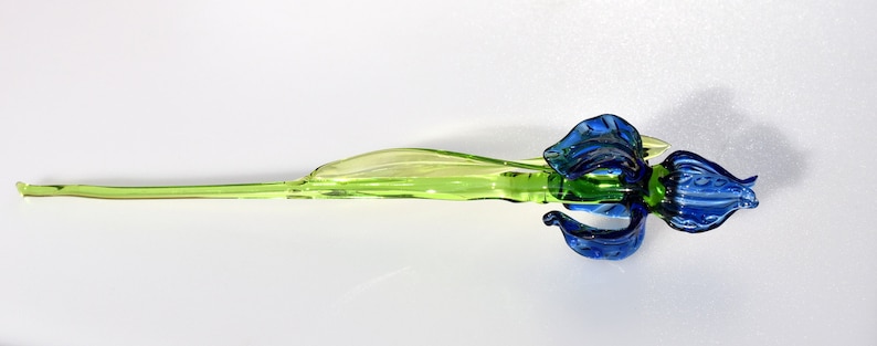 May include: A glass sculpture of a blue iris flower with a green stem.