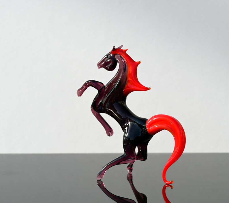 Peut inclure: Une figurine de cheval en verre noir avec une crini&egrave;re et une queue rouges. Le cheval se dresse sur ses pattes arri&egrave;re.