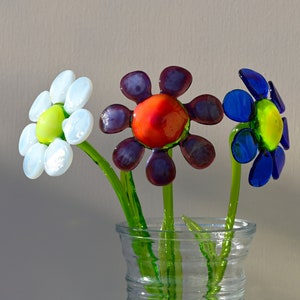 May include: Three glass flowers in a clear vase. The flowers are white, purple and blue with red centres.