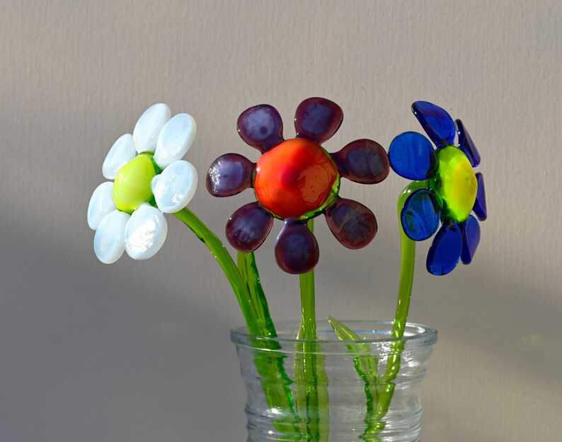 May include: Three glass flowers in a clear vase. The flowers are white, purple and blue with red centres.