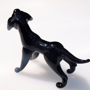 May include: A black glass sculpture of a dog standing on all four legs. The dog is looking up and has a long tail.