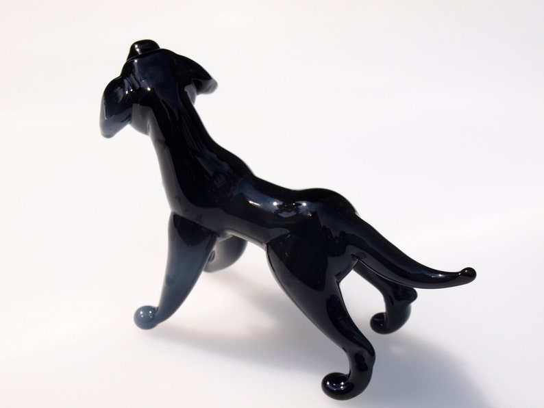 May include: A black glass sculpture of a dog standing on all four legs. The dog is looking up and has a long tail.