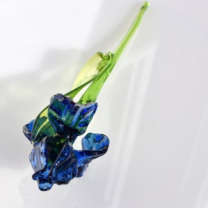 May include: A blue glass flower with green stem. The flower is made of glass and has a delicate, realistic appearance.