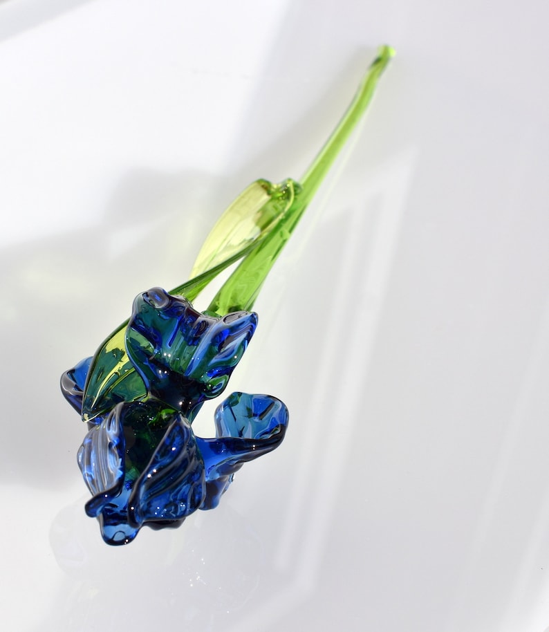 May include: A blue glass flower with green stem. The flower is made of glass and has a delicate, realistic appearance.