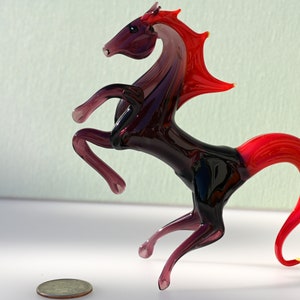 Peut inclure: Une figurine de cheval en verre dans des tons de rouge et de violet, avec une queue et une crini&egrave;re relev&eacute;es. Le cheval se tient sur ses pattes arri&egrave;re, ses pattes avant &eacute;tant tendues vers l'avant.