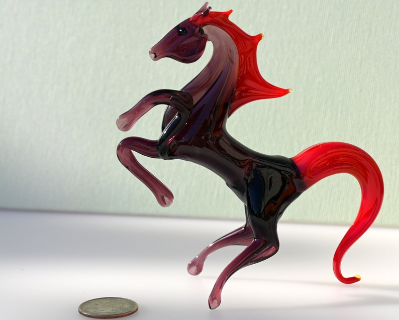 Peut inclure: Une figurine de cheval en verre dans des tons de rouge et de violet, avec une queue et une crini&egrave;re relev&eacute;es. Le cheval se tient sur ses pattes arri&egrave;re, ses pattes avant &eacute;tant tendues vers l'avant.