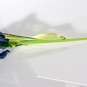May include: A glass flower sculpture with a blue and green iris bloom and a long, green stem.