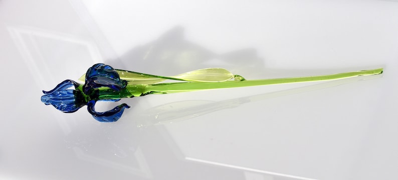 May include: A glass flower sculpture with a blue and green iris bloom and a long, green stem.