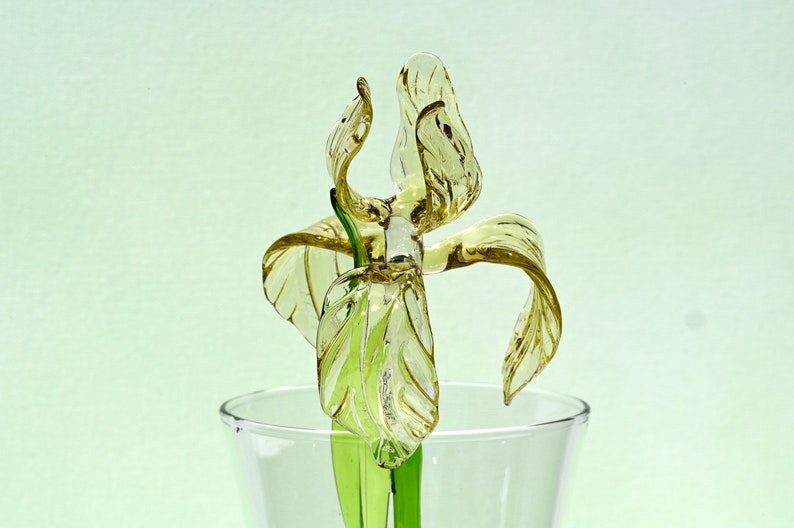 May include: A glass sculpture of a yellow iris flower with green stem in a clear glass vase.