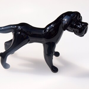 May include: A black glass sculpture of a dog in a walking pose. The dog has a long snout and a short tail.
