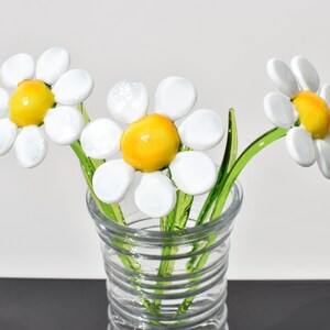 May include: Three white glass daisies with yellow centers in a clear glass vase with a spiral pattern.