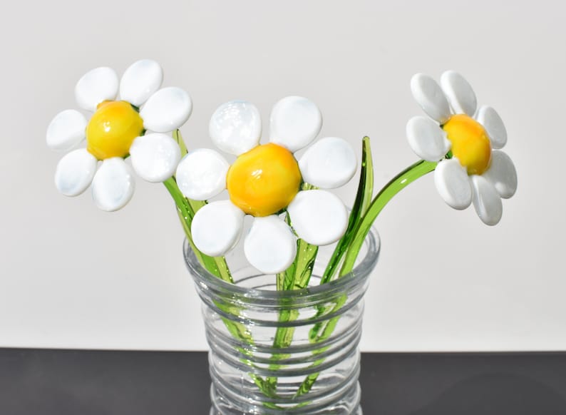 May include: Three white glass daisies with yellow centers in a clear glass vase with a spiral pattern.