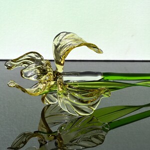 May include: A glass flower sculpture with a yellow flower and green stem. The flower is made of glass and has a delicate, intricate design. The stem is also made of glass and is a vibrant green color.