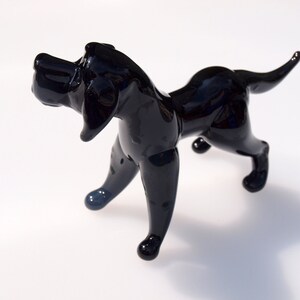 May include: A black glass sculpture of a dog. The dog is standing on all four legs and has its head tilted to the side. The sculpture is made of clear glass with a black finish.