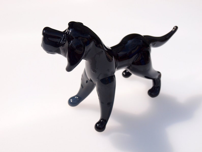May include: A black glass sculpture of a dog. The dog is standing on all four legs and has its head tilted to the side. The sculpture is made of clear glass with a black finish.