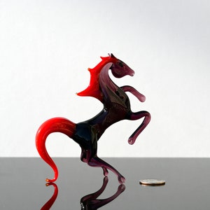 Peut inclure: Une figurine de cheval en verre avec une crini&egrave;re et une queue rouges, debout sur ses pattes arri&egrave;re. Le cheval est de couleur violet fonc&eacute; avec un corps noir.