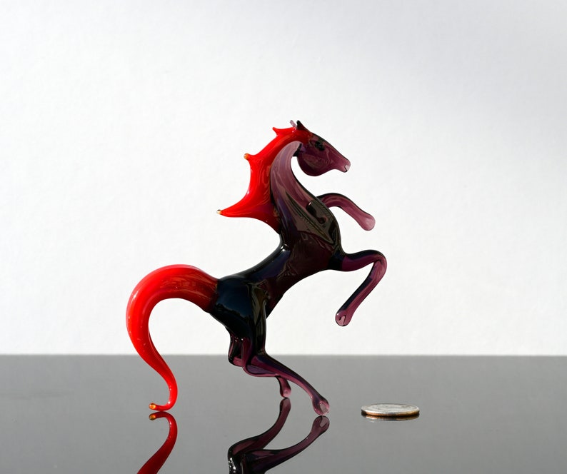 Peut inclure: Une figurine de cheval en verre avec une crini&egrave;re et une queue rouges, debout sur ses pattes arri&egrave;re. Le cheval est de couleur violet fonc&eacute; avec un corps noir.