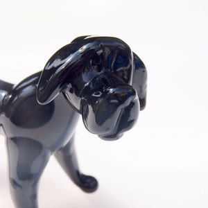 May include: A black glass sculpture of a dog. The dog is standing on all four legs and has a long snout. The sculpture is made of a smooth, shiny glass.