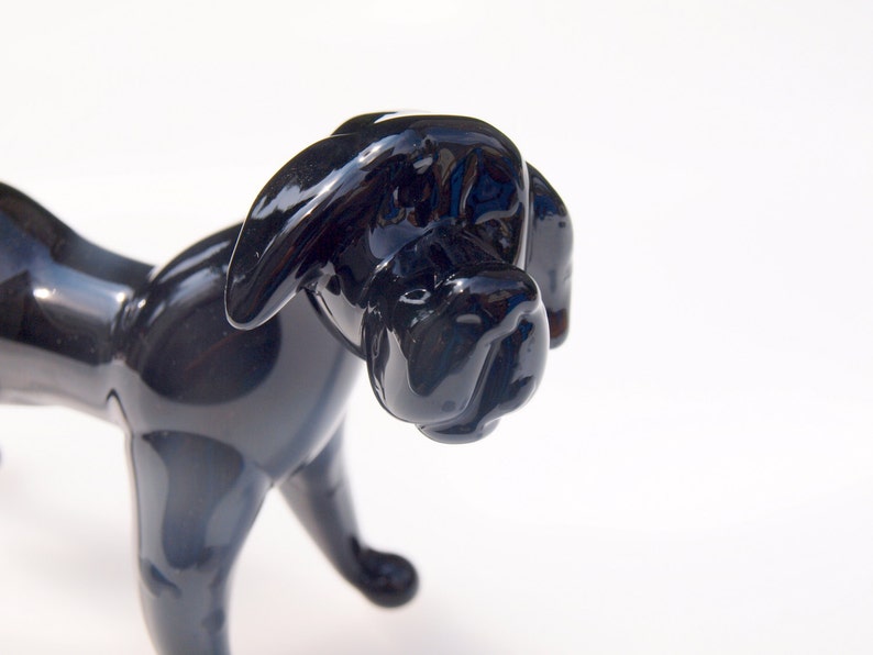 May include: A black glass sculpture of a dog. The dog is standing on all four legs and has a long snout. The sculpture is made of a smooth, shiny glass.
