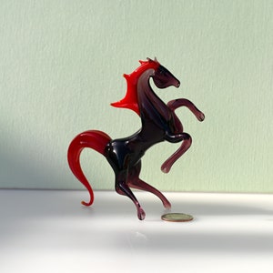 Peut inclure: Une figurine de cheval en verre se cabrant avec une crini&egrave;re et une queue rouges. Le cheval est de couleur violet fonc&eacute; et pr&eacute;sente un design d&eacute;taill&eacute;.