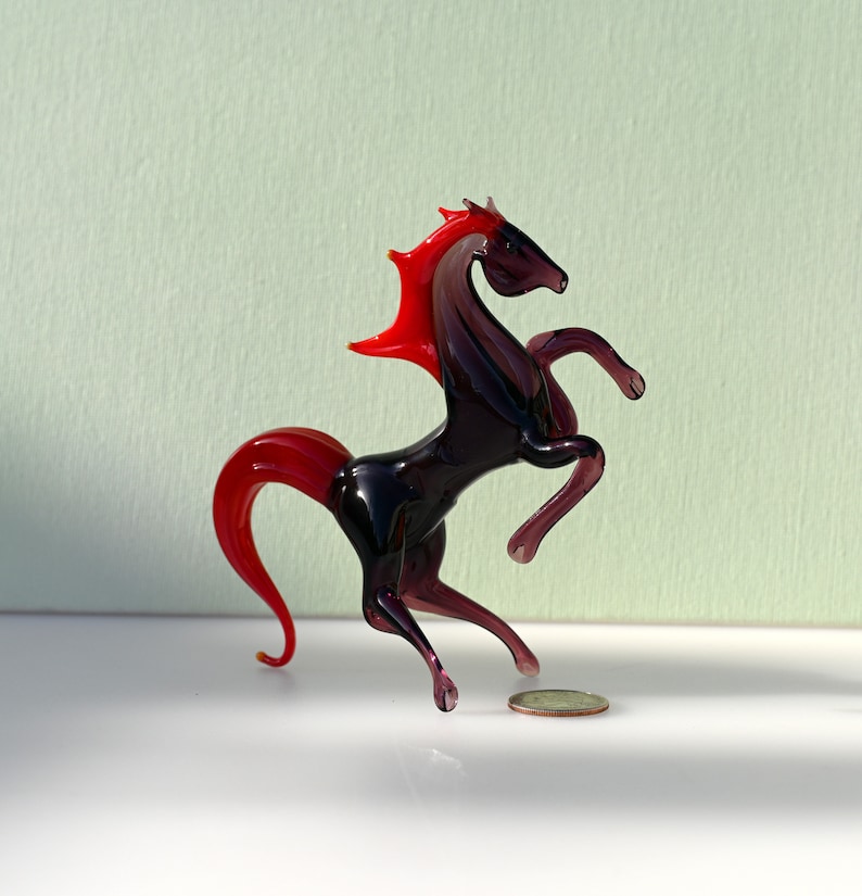 Peut inclure: Une figurine de cheval en verre se cabrant avec une crini&egrave;re et une queue rouges. Le cheval est de couleur violet fonc&eacute; et pr&eacute;sente un design d&eacute;taill&eacute;.