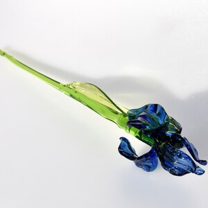 May include: A glass sculpture of a blue iris flower with a green stem.