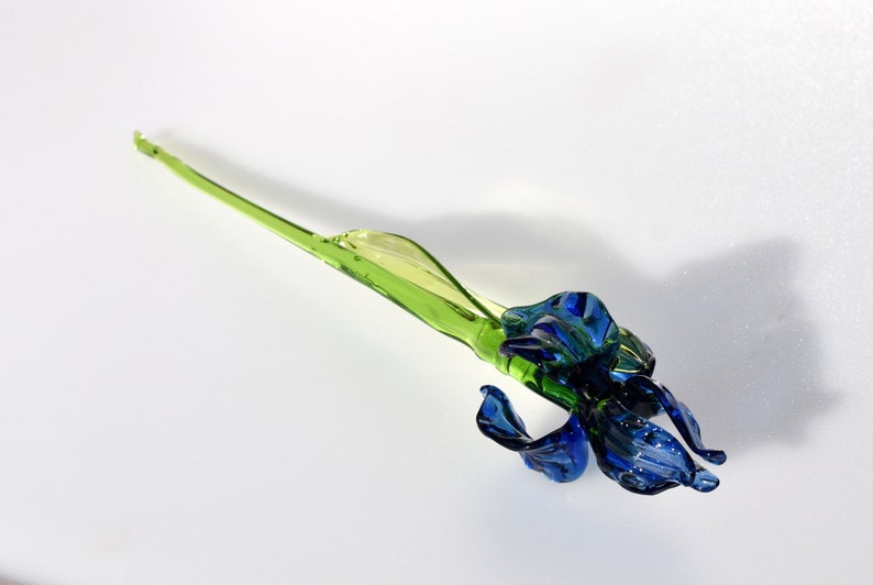 May include: A glass sculpture of a blue iris flower with a green stem.