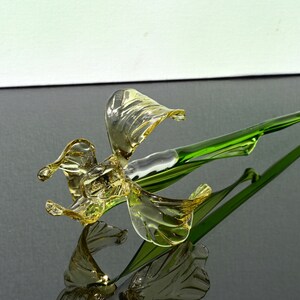 May include: A glass flower sculpture with a yellow flower and a green stem. The flower is made of blown glass and has a delicate, intricate design.
