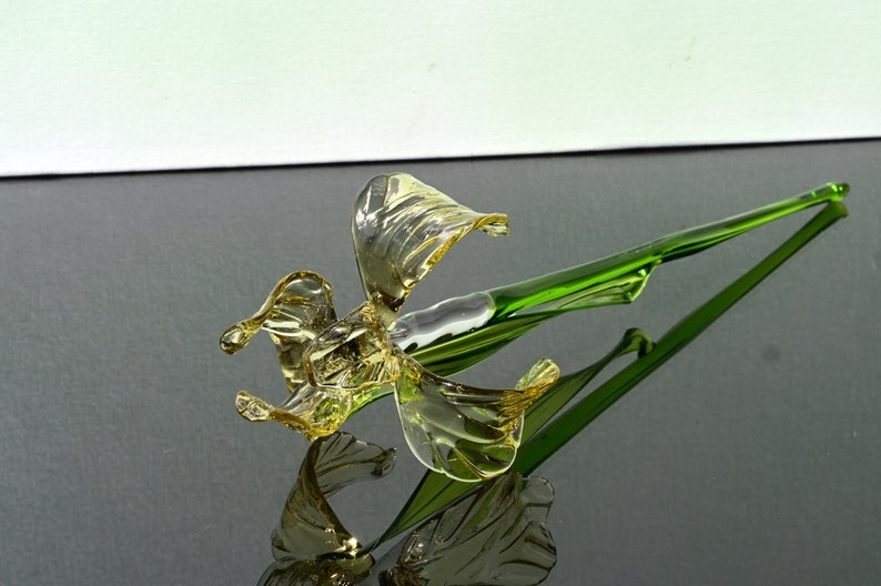 May include: A glass flower sculpture with a yellow flower and a green stem. The flower is made of blown glass and has a delicate, intricate design.