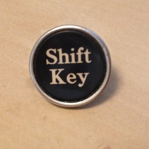 May include: A black and white round keycap with the words "Shift Key" printed on it.