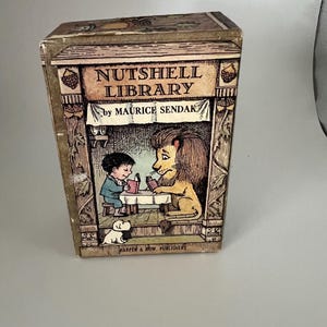 May include: A vintage "Nutshell Library" box set by Maurice Sendak. The box features a detailed illustration of a boy and a lion reading at a table, with a small dog. The box is tan with a decorative border and the publisher's name.