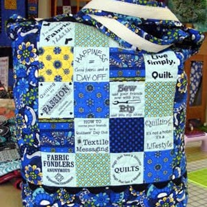 May include: A quilted tote bag featuring a patchwork design of blue, yellow, and white fabric squares. The squares display various floral patterns, polka dots, and text including "Happiness = Good fabric and a DAY OFF" and "Quilting is my PASSION."