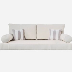 May include: A modern, off-white sofa with two square back cushions and two striped accent pillows. Two cylindrical bolsters are on either end. The pillows have gray and white stripes. The sofa is a neutral color.