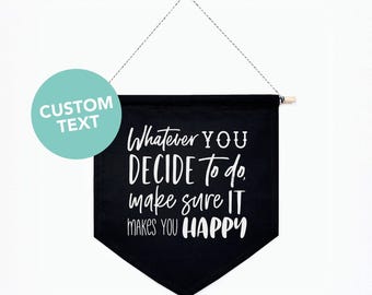 May include: A black fabric wall banner with a pointed bottom edge, suspended by a string from a wooden dowel. The banner features white text that reads: Whatever YOU DECIDE To do, make sure IT MAKES YOU HAPPY. A teal circle with CUSTOM TEXT is visible.