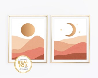 May include: Two framed wall art prints featuring layered desert landscapes in shades of peach, terracotta, and brown. One print displays a metallic gold sun, while the other shows a metallic gold crescent moon and stars. A circular gold seal reads MULTIPLE REAL FOIL COLORS AVAILABLE.