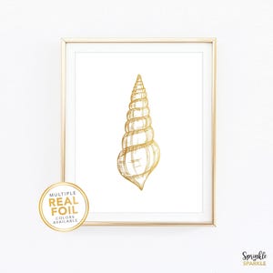 May include: A framed print featuring a gold foil illustration of a seashell on a white background. The artwork is encased in a gold frame. A circular sticker in the lower left corner reads "MULTIPLE REAL FOIL COLORS AVAILABLE."