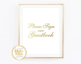 Puede incluir: Un letrero blanco enmarcado con texto dorado que dice "Please Sign our Guestbook". El letrero está en un marco dorado y tiene una pegatina dorada en la esquina inferior izquierda. La pegatina dice "Multiple Real Foil Colors Available".