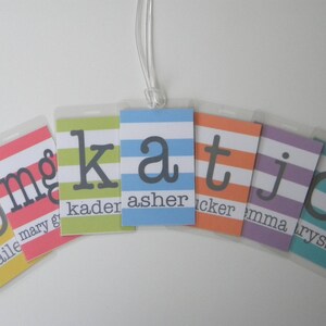May include: Six colorful striped luggage tags with the letters b, m, g, k, a, t, j, and c in black. The tags are labeled with the names Bailey, Mary, Kaden, Asher, Tucker, Emma, and Lyss.