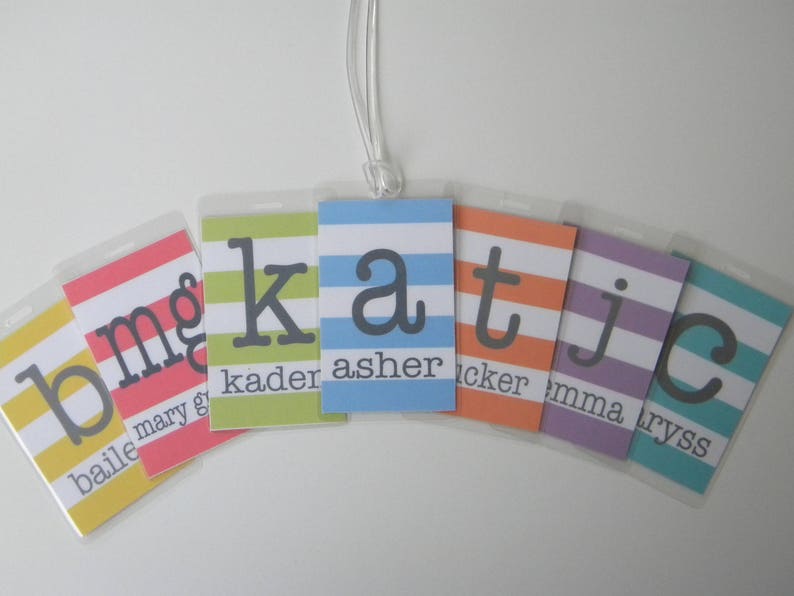 May include: Six colorful striped luggage tags with the letters b, m, g, k, a, t, j, and c in black. The tags are labeled with the names Bailey, Mary, Kaden, Asher, Tucker, Emma, and Lyss.