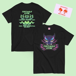 Puede incluir: Dos camisetas negras con gráficos en verde neón y rosa. Una camiseta presenta un gato estilizado con el texto "TRITAILS GYM". La otra muestra "TRITAILS GYM" y "HOME OF THE FAMOUS - TRITAILS TRAINING TRIO - BLOCK M-1 TRUE VIEW RESIDENTIAL DISTRICT".