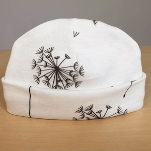 May include: White beanie hat with a black dandelion design. The hat features a rolled-up brim and a repeating pattern of dandelion seed heads. The hat is made of a soft, lightweight fabric.