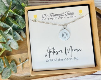 May include: A silver necklace with a puzzle piece pendant in a gift box. The box has a white card with the text "Autism Mama Until All the Pieces Fit."