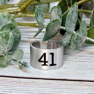 May include: A silver metal ring with the number 41 engraved on it. The ring is sitting on a wooden surface.