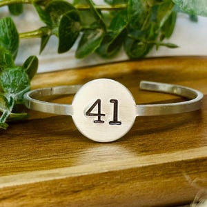 May include: Silver bracelet with a round charm featuring the number 41.