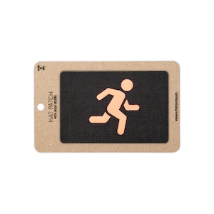 May include: A rectangular black hat patch with hook velcro backing, featuring a peach-colored graphic of a person running. The patch is mounted on a tan cardboard display card printed with the text HAT PATCH WITH HOOK VELCRO and MADE IN USA.