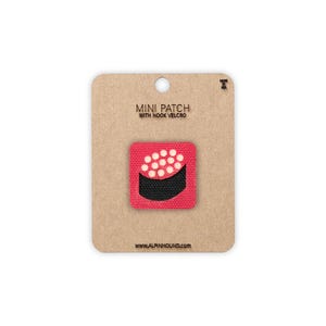 May include: A mini patch with hook and loop fastening, featuring a red square with a sushi design. The sushi has a black base and white circular details. The patch is attached to a brown card with the text "MINI PATCH WITH HOOK VELCRO" and the website address.