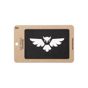 May include: A rectangular black hat patch with a white graphic of an owl with spread wings. The patch is mounted on a tan cardboard backing card that features the text HAT PATCH WITH HOOK VELCRO, MADE IN USA, and www.alphahound.com.