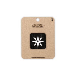 May include: A mini patch with hook velcro, featuring a white starburst design on a black square. The patch is attached to a brown cardboard backing with the text "MINI PATCH WITH HOOK VELCRO" and "WWW.ALPINHOUND.COM".